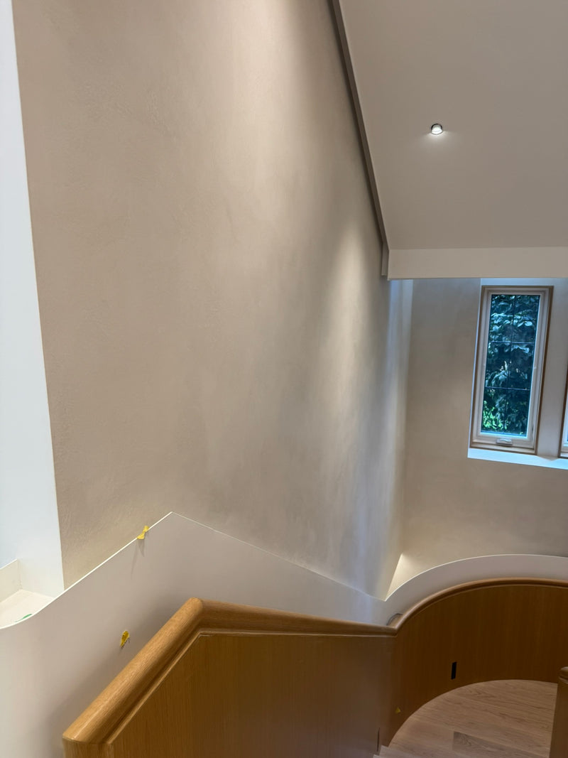 Softly lit Carrara Marmorino plaster walls above a curved wooden stair railing